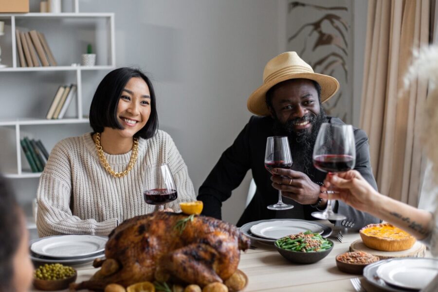 Positive multiethnic couple drinking wine with guests